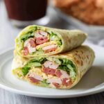 A delicious California turkey club wrap cut in half, filled with sliced turkey, crispy bacon, fresh lettuce, tomato, and cheese, all wrapped in a soft tortilla.