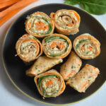 Whole wheat wraps rolled with turkey, cheese, shredded carrots, and spinach, sliced into bite-sized pinwheels and served on a black plate.