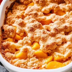 Close-up of a golden-brown peach cobbler in a white baking dish with bubbly, juicy peach filling and a crumbly, buttery topping.