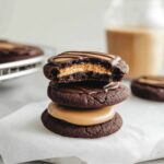 A stack of rich chocolate Buckeye Cookies with a creamy peanut butter center, one with a bite taken out, drizzled with melted chocolate.