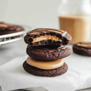 A stack of rich chocolate Buckeye Cookies with a creamy peanut butter center, one with a bite taken out, drizzled with melted chocolate.