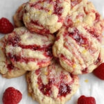 Freshly baked lemon raspberry cookies with vibrant red raspberry swirls and a sugar-dusted top, surrounded by whole raspberries.