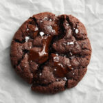 Close-up of a single double chocolate cookie with gooey melted chocolate and a sprinkle of sea salt on top.