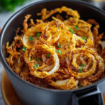 Golden, crispy onion rings made in the air fryer, served in a black bowl with fresh parsley garnish.