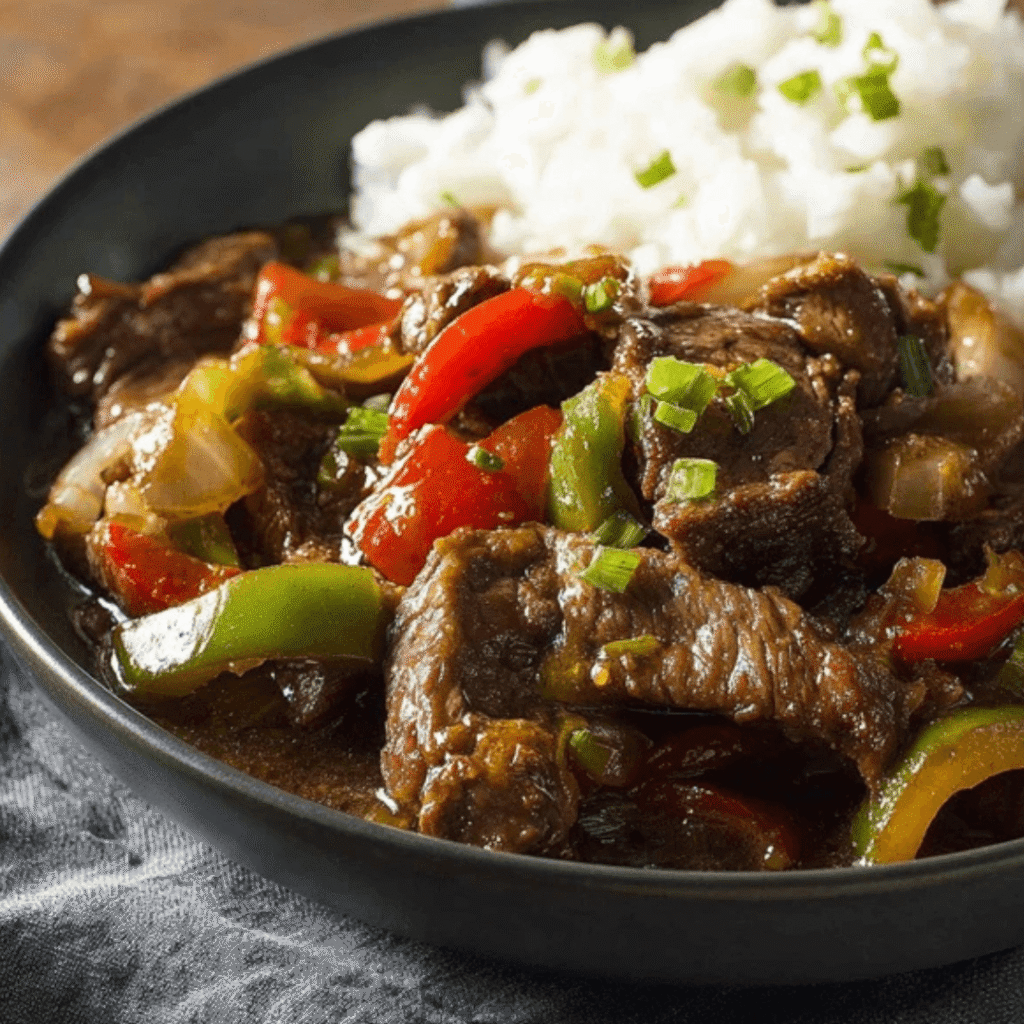 A savory bowl of crockpot pepper steak with tender beef strips, colorful bell peppers, onions, and rich sauce served alongside fluffy white rice.