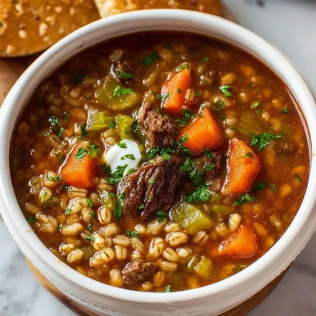 Slow Cooker Beef Barley Soup in a bowl with tender beef, pearl barley, carrots, celery, and fresh parsley, steaming hot and ready to serve.