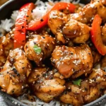 Black Pepper Chicken with rice and red bell peppers, garnished with sesame seeds in a bowl.