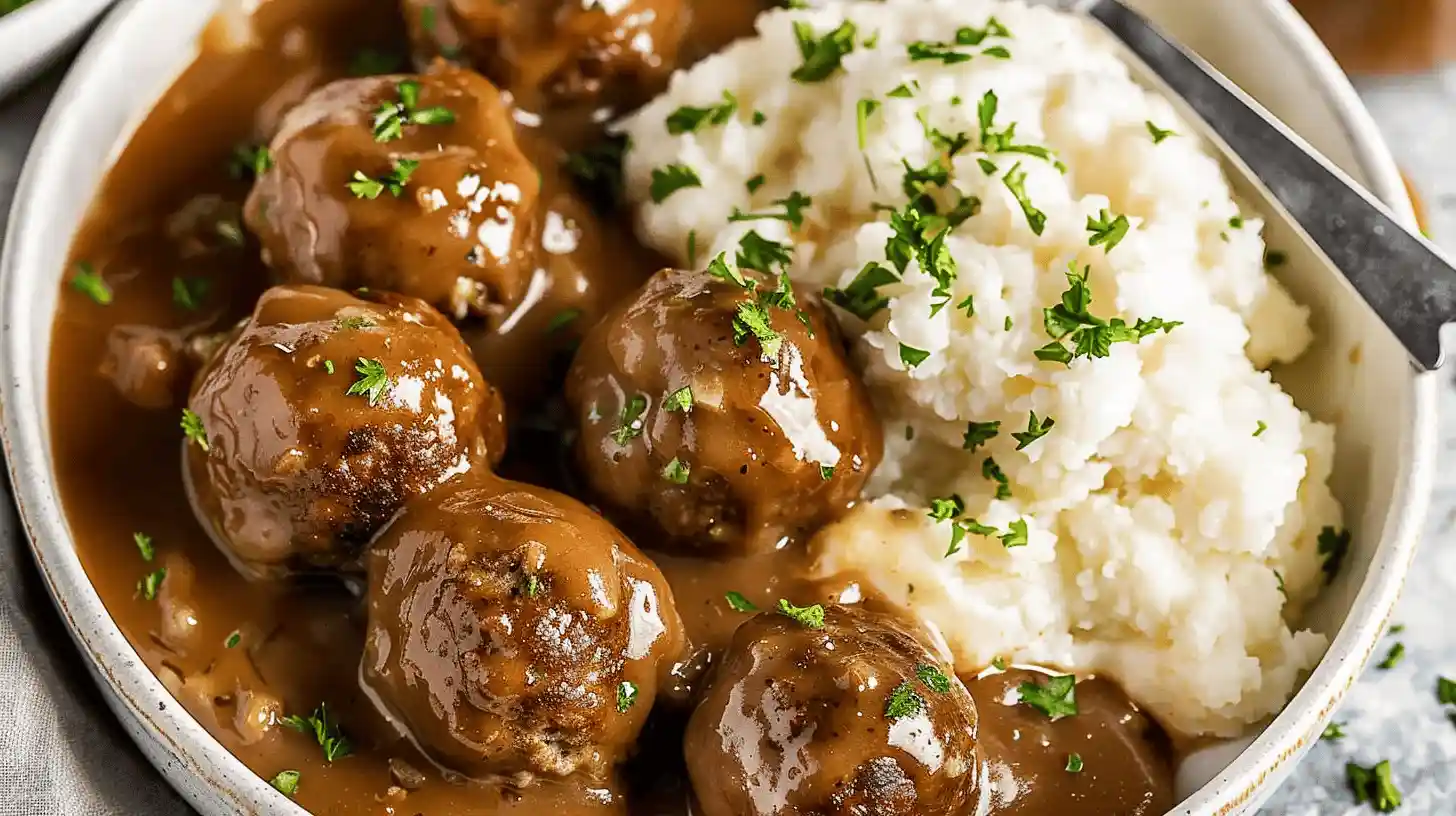 Plate of meatballs and gravy with mashed potatoes and herbs.