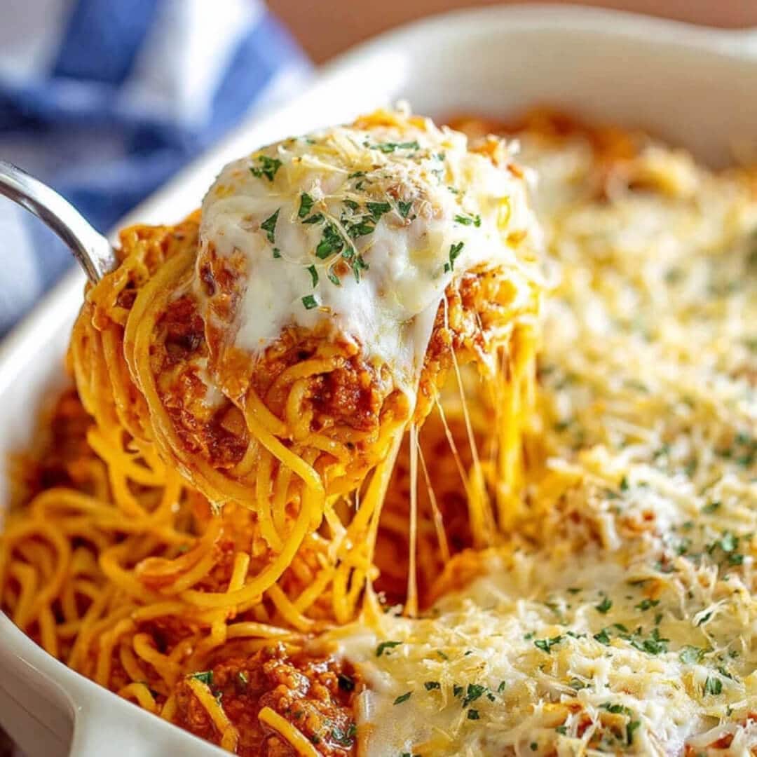 A dish of million dollar spaghetti topped with melted cheese and basil leaves.