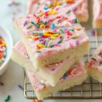 A close-up shot of a tray of freshly baked Sugar Cookie Bars, topped with smooth white frosting and colorful sprinkles.