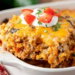 A bubbly, golden-brown Taco Casserole is presented in a baking dish, garnished with fresh cilantro and a dollop of sour cream.