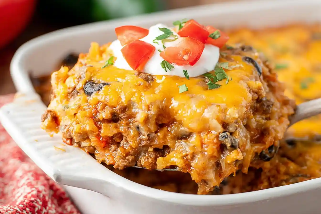 A bubbly, golden-brown Taco Casserole is presented in a baking dish, garnished with fresh cilantro and a dollop of sour cream.
