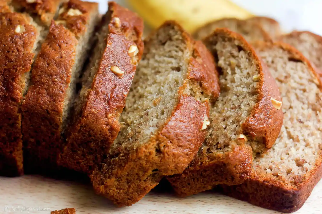 A perfectly baked, golden-brown loaf of Banana Bread sits on a wire cooling rack, garnished with a few banana slices.