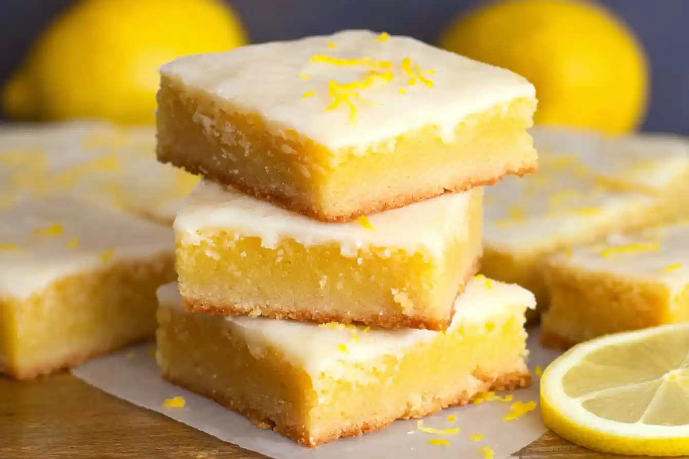 A close-up shows several golden-topped Lemon Brownie Bars Recipe squares dusted with powdered sugar, arranged on a serving platter.