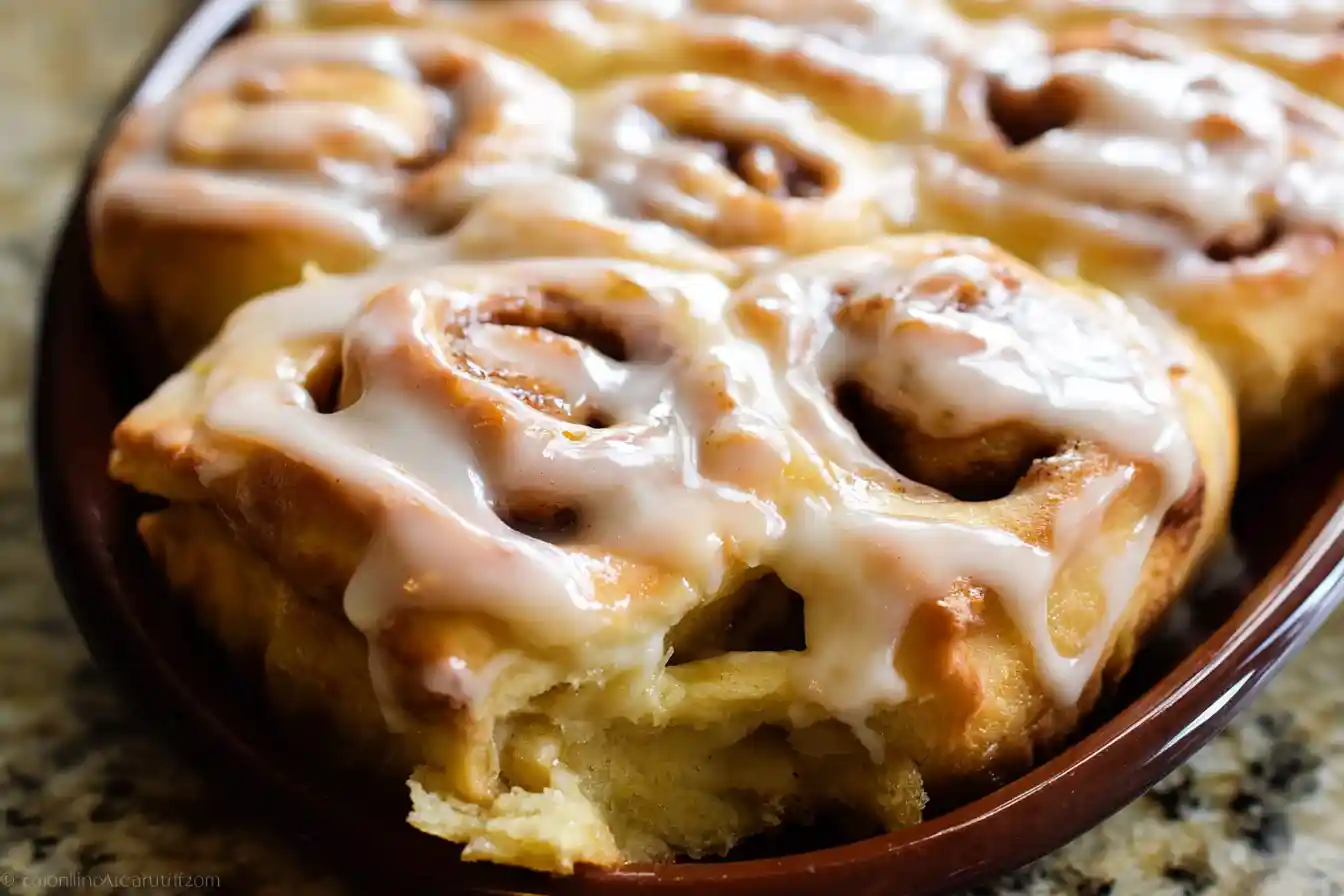 A close-up of a warm, freshly baked Apple Cinnamon Roll topped with sweet white glaze.