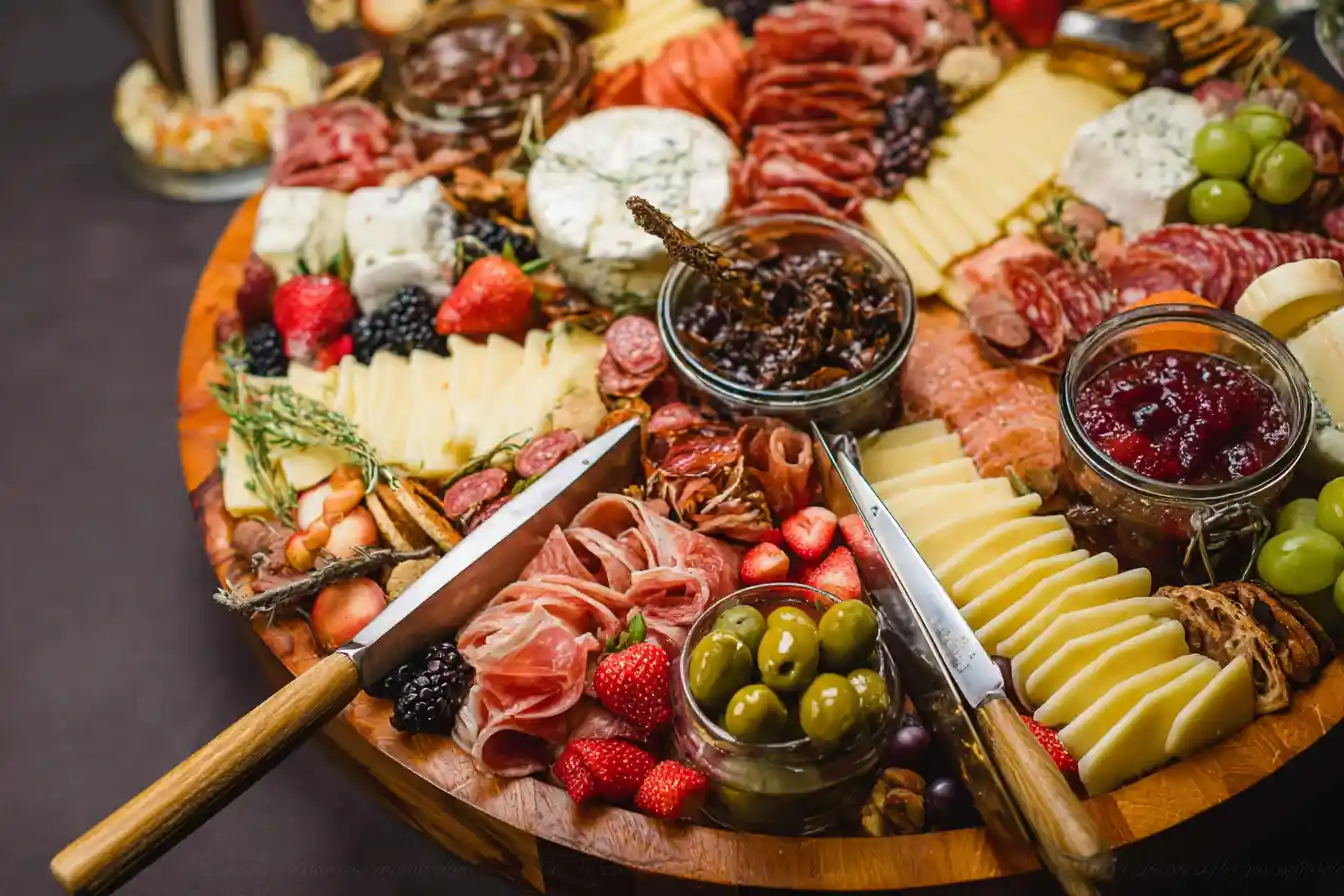 A vibrant and abundant charcuterie board featuring an assortment of cheeses, cured meats, fresh fruits, nuts, and crackers on a wooden surface.