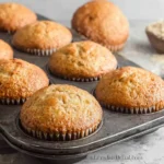 A close-up shot of several golden-brown Fluffy Banana Muffins with a perfectly domed top, cooling on a wire rack.