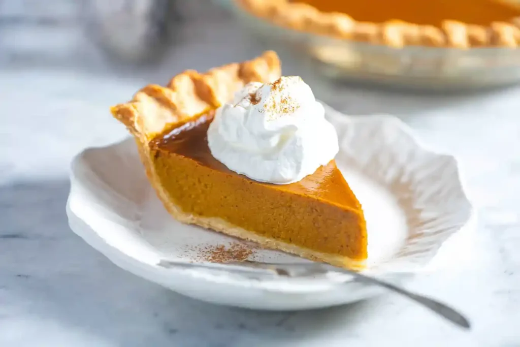 A perfectly baked pumpkin pie, with a golden-brown crust and smooth orange filling, rests on a counter, inspiring users to find a new pumpkin pie recipe.