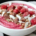 A vibrant Raspberry Coconut Crunch Bowl is beautifully arranged with fresh red raspberries, toasted coconut flakes, and a creamy, textured base.