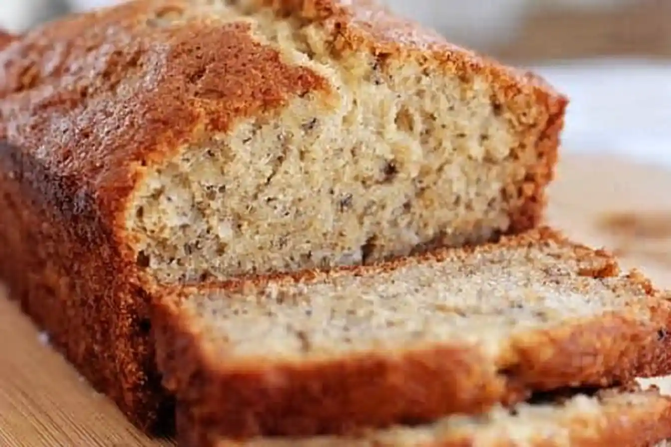 A close-up shot of a perfectly baked, golden-brown loaf of sour cream banana bread, sliced and presented on a wooden board.