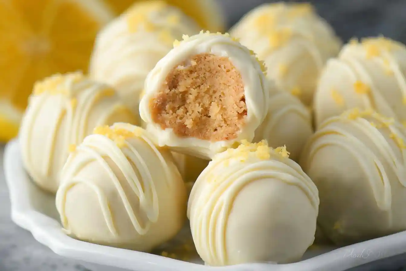 A close-up shot of white chocolate lemon truffles on a plate, with one cut in half to show the cake-like center.
