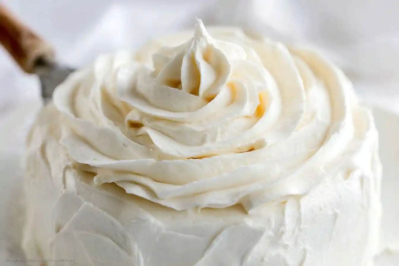 A close-up of a white cake beautifully decorated with thick, fluffy swirls of homemade cream cheese frosting.