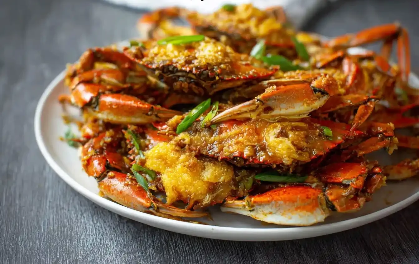A white plate piled high with delicious homemade Stir Fried Crab, garnished with fresh green scallions on a dark wooden table.