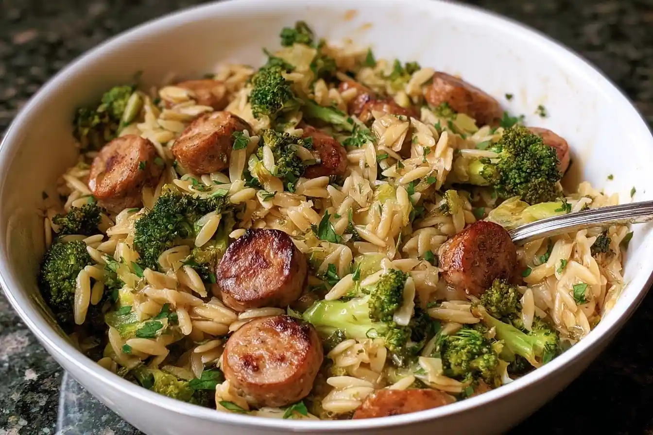A close-up of a white bowl filled with delicious sausage and broccoli orzo, garnished with fresh parsley and ready to eat.