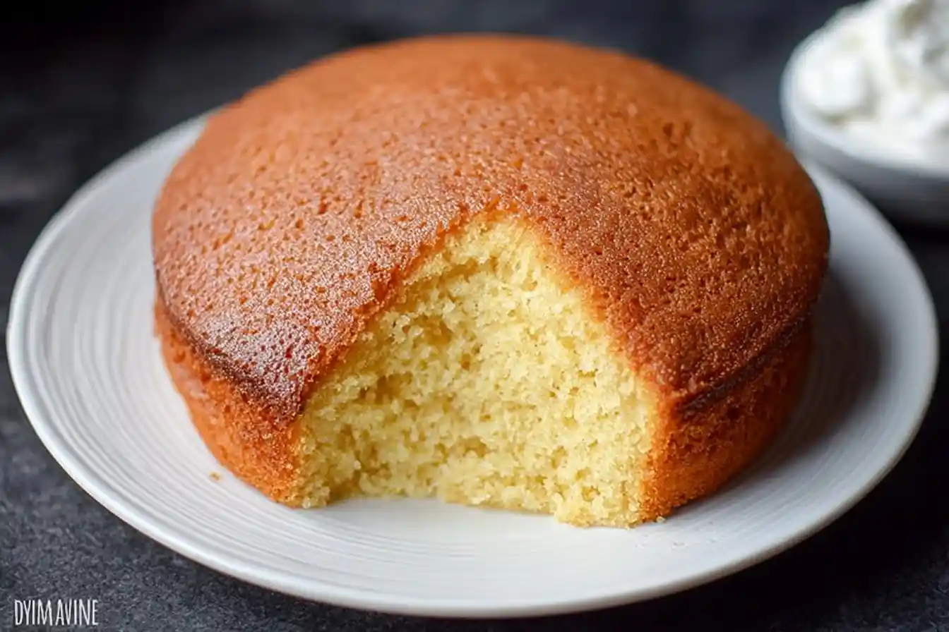 A freshly baked vanilla sponge cake with a slice removed, showcasing its light and fluffy crumb on a white plate.