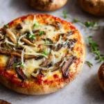 A close-up of a portobello mushroom pizza topped with melted cheese, sautéed mushrooms, and fresh thyme on parchment paper.