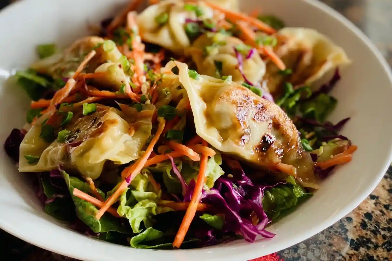 A close-up of a vibrant Dumpling Salad with pan-fried potstickers, shredded carrots, and cabbage in a white bowl.