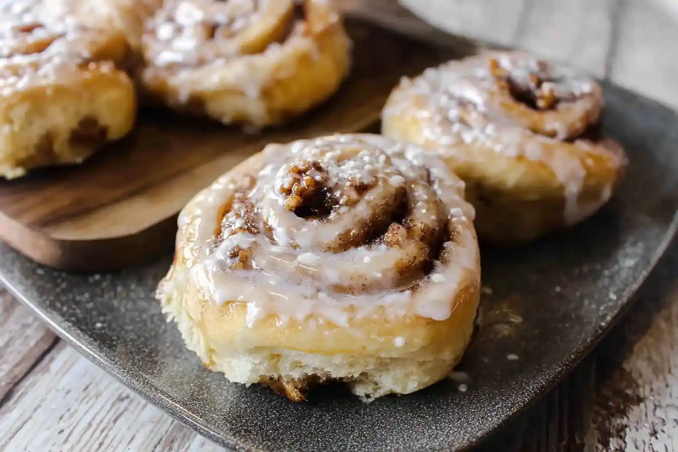A close-up of delicious {{ $('Fetch Recipe Data').first().json["Main Keyword"] }} with icing, served on a rustic gray plate and wooden board.