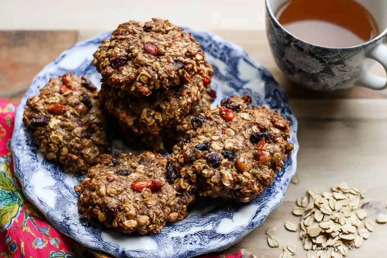A blue and white plate piled with delicious healthy oatmeal cookies, served with a cup of hot tea on a wooden table.