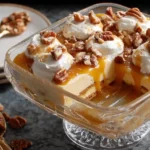 Glass dish serving a creamy Caramel Pecan Delight topped with whipped cream, caramel sauce, and nuts.