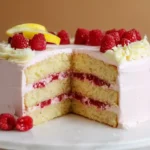 Sliced lemon raspberry cake on a white stand, showcasing fluffy layers, raspberry filling, and fresh fruit toppings.
