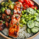 Top view of a Teriyaki Salmon Bowl with glazed salmon, broccoli, mushrooms, edamame, and cucumber over rice.