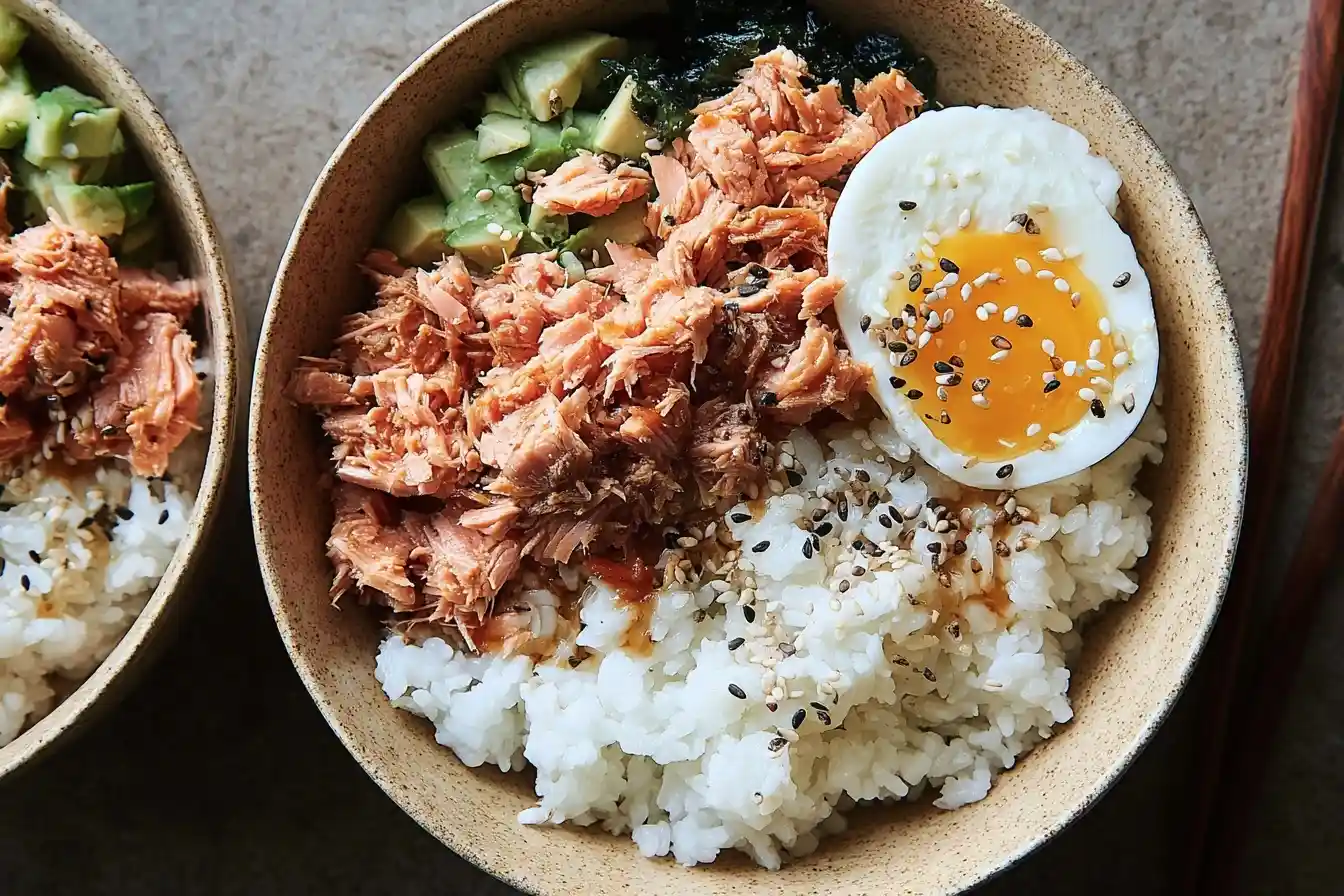 Top-down view of a salmon rice bowl topped with flaked salmon, avocado, seaweed, and a soft-boiled egg.