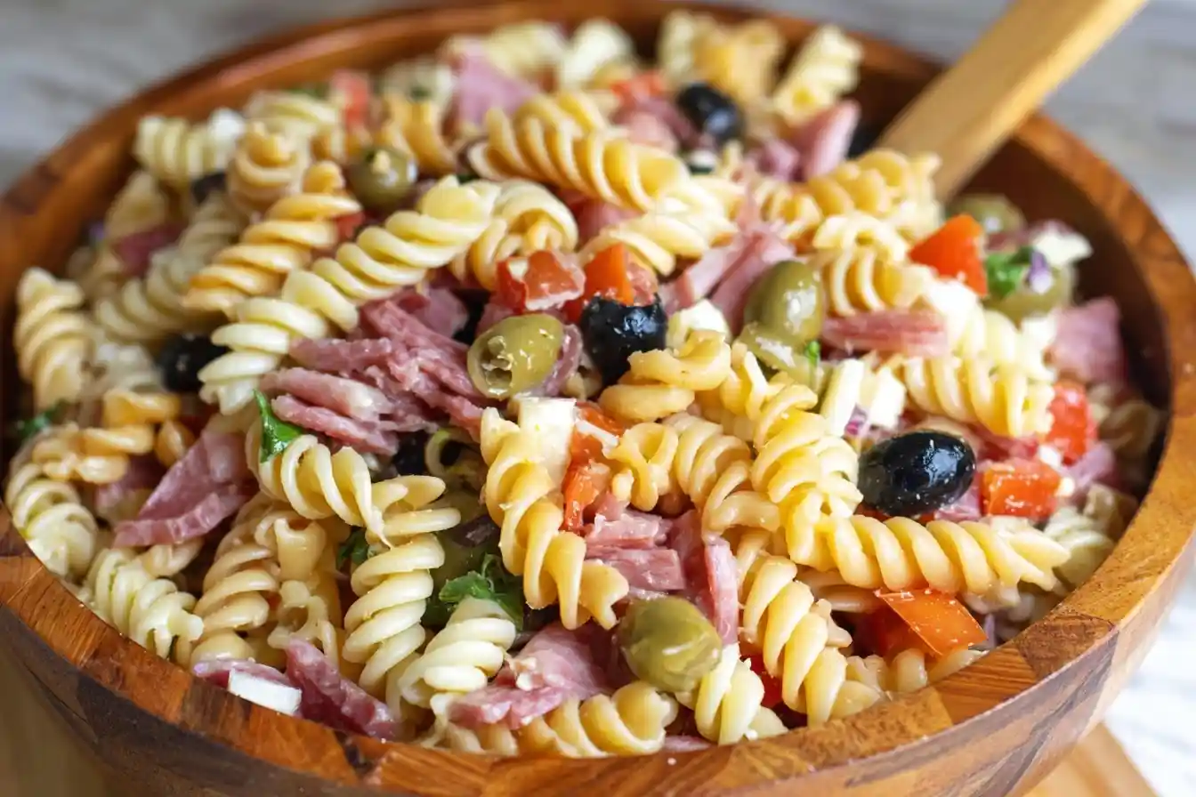 Close-up of a colorful Italian pasta salad with rotini, salami, olives, and peppers in a wooden bowl