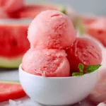 Three scoops of refreshing pink watermelon sorbet in a white bowl garnished with fresh mint.