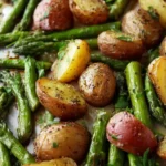 Close-up of a baking sheet with golden roasted potatoes and asparagus coated in fresh herbs.