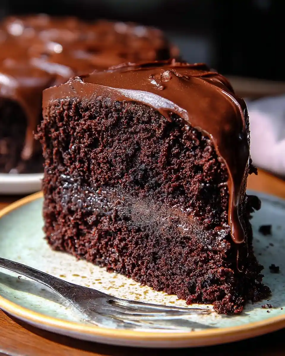 Close-up of a rich {{ $('Fetch Recipe Data').first().json["Main Keyword"] }} slice with thick glossy chocolate frosting on a plate.