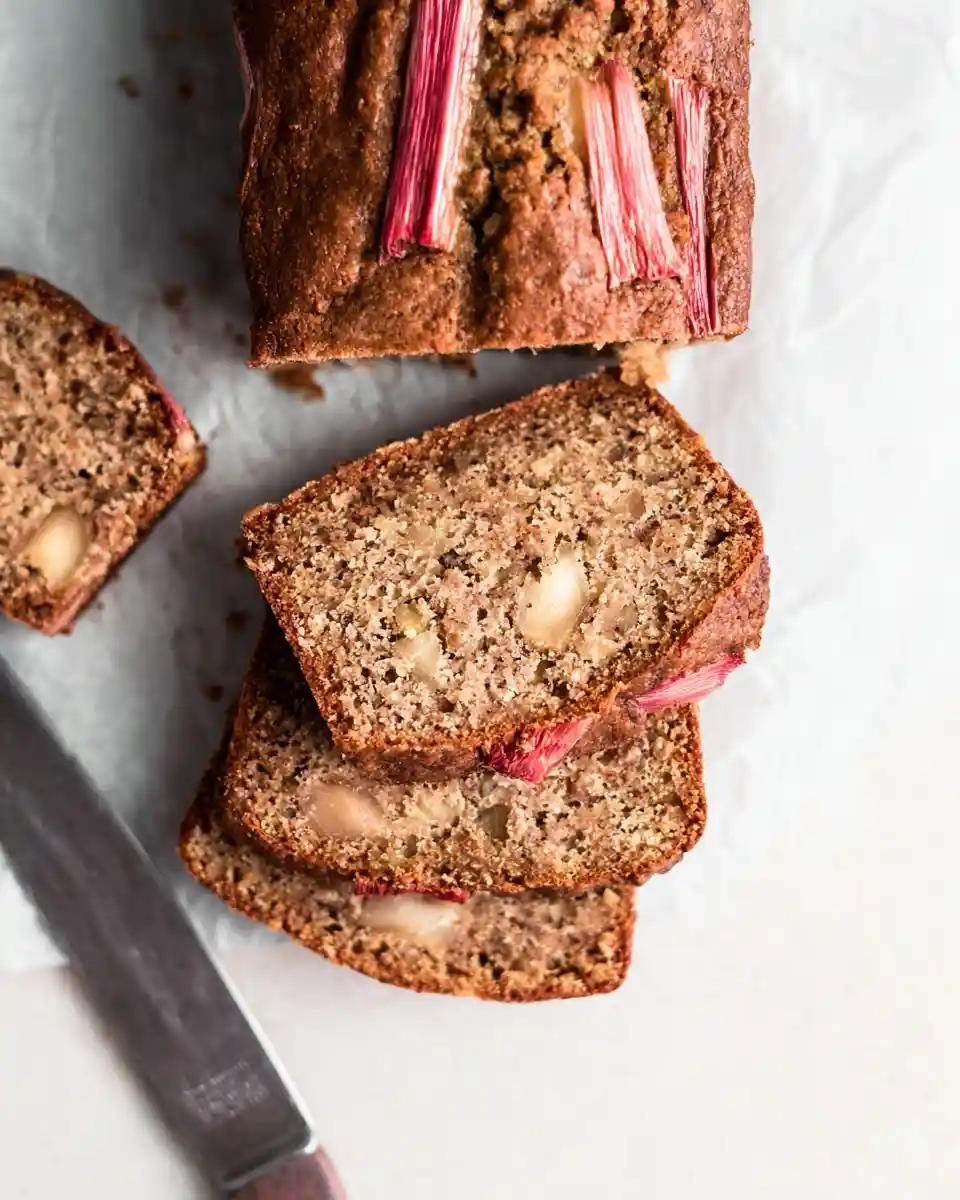 Top-down view of sliced rhubarb bread with pink stalks baked on top, resting on parchment paper.