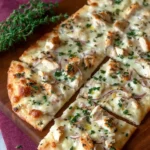 Sliced chicken flatbread topped with melted cheese, chicken, red onion, and thyme on a wooden board.