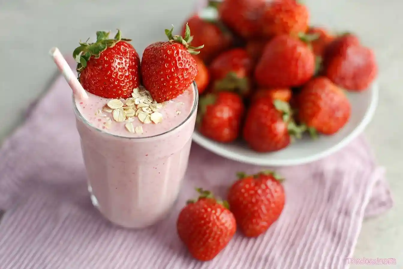 Glass of pink strawberry oatmeal smoothie garnished with oats and fresh berries on a pink napkin.