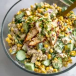 A glass bowl filled with creamy chicken corn salad, topped with sliced grilled chicken breast and fresh dill garnish.