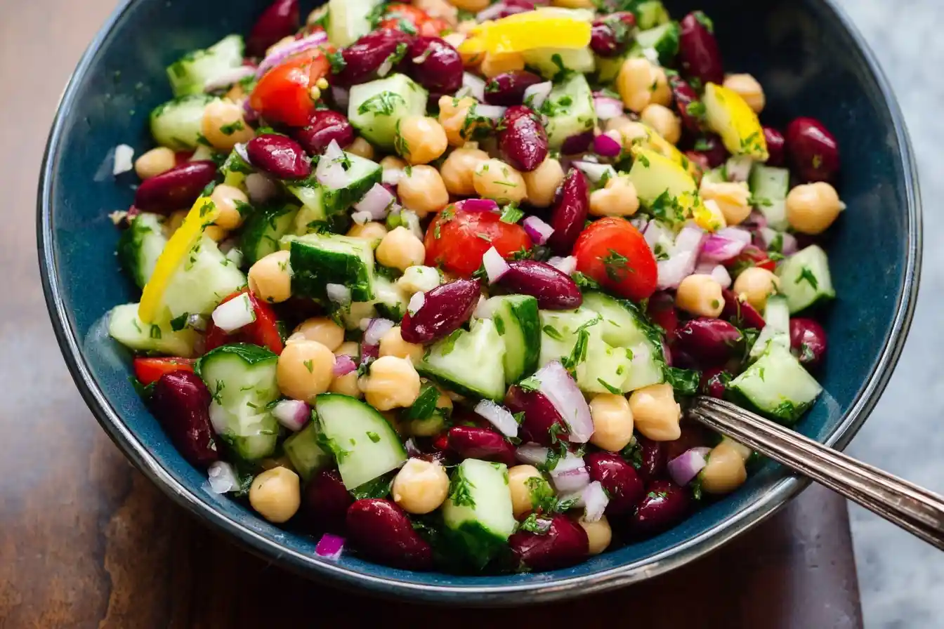 Close-up overhead shot of a colorful bean salad with chickpeas, kidney beans, and cucumber in a blue bowl.