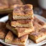 A stack of freshly baked {{ $('Fetch Recipe Data').first().json["Main Keyword"] }} topped with cinnamon sugar on a white plate.