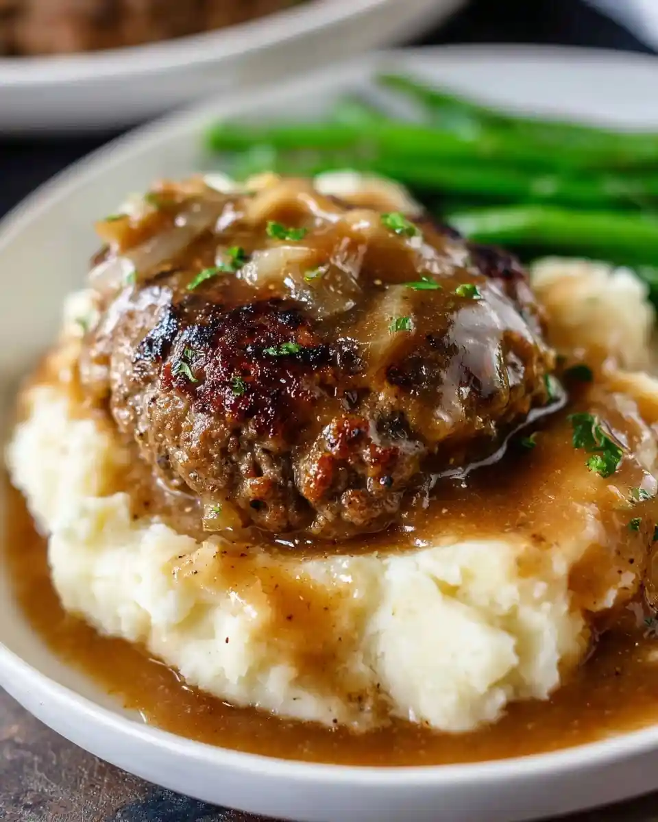 A delicious Salisbury steak topped with brown onion gravy, served over a bed of creamy mashed potatoes.