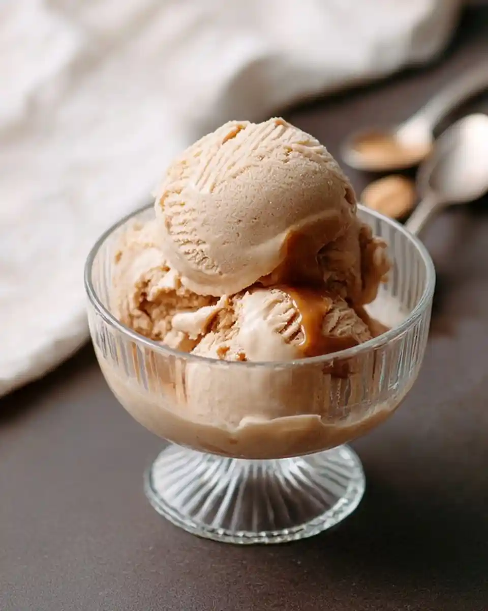 Three scoops of creamy coffee ice cream topped with a rich caramel drizzle in a glass dessert bowl.