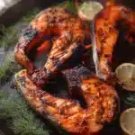 Grilled salmon collars on a plate with herbs and lemon garnish